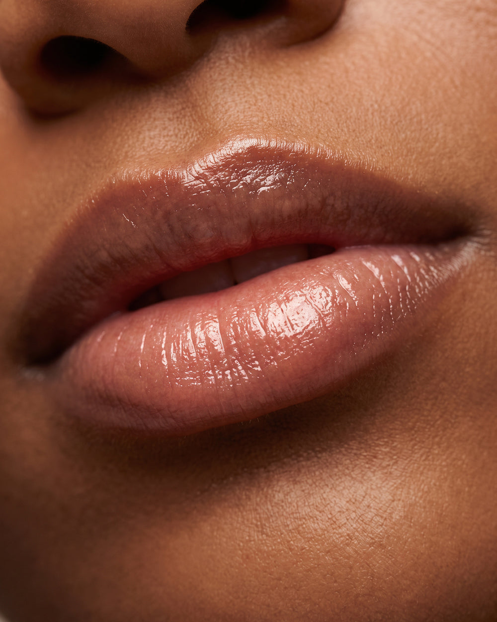 A close-up of softly parted lips with a glossy, natural finish on a woman with a deep skin tone.