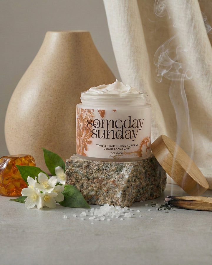 Someday Sunday Cedar Sanctuary body cream open on stone beside a vase and drifting incense.