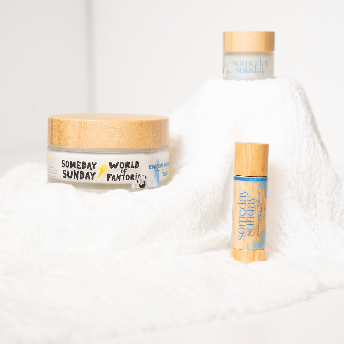 The Seen trio: a 3 oz Big Blue Seen body cream, a lip butter jar and a lip butter stick on soft white linen.