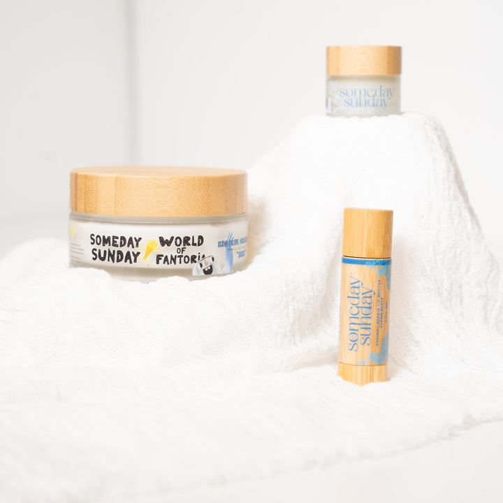 The Seen trio: a 3 oz Big Blue Seen body cream, a lip butter jar and a lip butter stick on soft white linen.