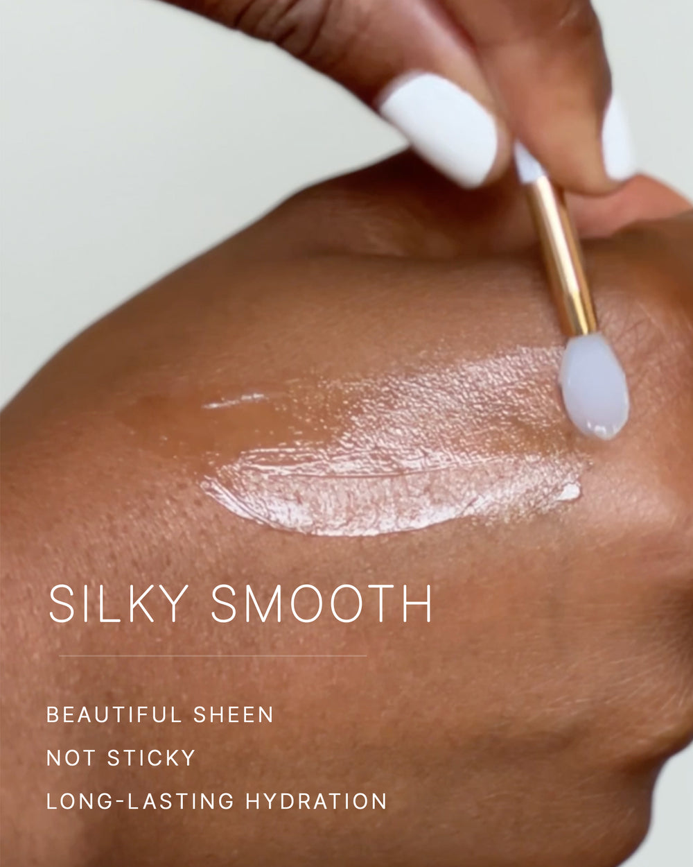 Silky smooth. Beautiful sheen. Not sticky. Long-lasting hydration. A hand with white nails swipes a stroke of lip butter across deep-toned skin, leaving a soft sheen.